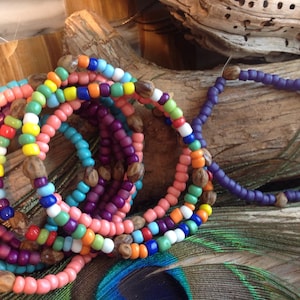 Peut inclure: Une collection de bracelets de perles composés de perles en verre multicolores dans des tons de rose, bleu, vert, jaune, orange et violet, entrecoupées de petites perles de graines naturelles brunes et texturées disposées en cercles.