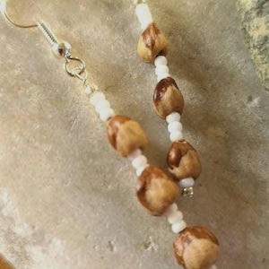 Peut inclure: Boucles d'oreilles faites à la main avec des perles en forme de glands de couleur marron clair, alternant avec de petites perles blanches. Les boucles ont des crochets d'oreilles et des attaches argentés.