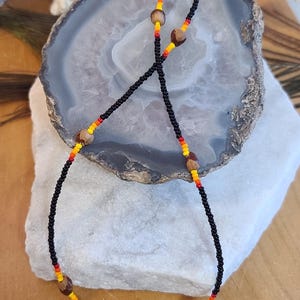 May include: A black beaded necklace with red, yellow, and orange accents and brown wooden beads.