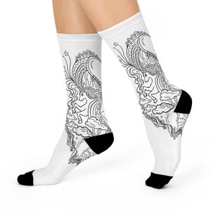 May include: A pair of white socks with a black and white line drawing of a unicorn on each sock. The unicorn is surrounded by clouds, stars, and a rainbow.