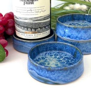 May include: Four blue ceramic coasters with a white and blue marbled design. The coasters are stacked on top of each other. The top coaster is slightly tilted. The coasters are on a white surface.