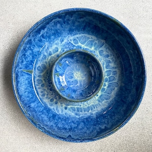 May include: A two-piece ceramic serving set with a vibrant blue glaze. The set includes a large, shallow dish and a smaller, round bowl that fits inside. The glaze has a marbled effect with lighter blue and white accents, creating a unique, artistic look.