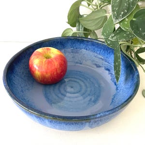 May include: A large, blue ceramic bowl with a swirling glaze pattern. An apple sits in the center of the bowl.