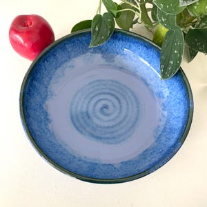 May include: A large, blue and white ceramic bowl with a swirl design. The bowl has a dark blue rim and a light blue glaze.
