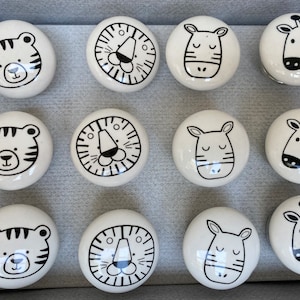Peut inclure: Dix boutons en céramique blanche avec des illustrations d'animaux noirs. Les animaux comprennent un tigre, un zèbre, une girafe et un lion. Les boutons sont ronds et ont une surface lisse.