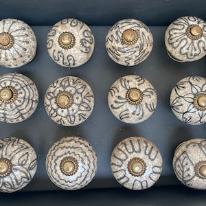 May include: Twelve ceramic drawer knobs with a white background and black intricate designs. Each knob has a brass center.