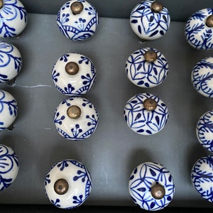 May include: A collection of 14 blue and white ceramic drawer knobs with intricate floral and geometric patterns. The knobs have a gold-coloured metal accent in the centre.
