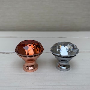 May include: Two diamond-shaped cabinet knobs, one with a copper finish and one with a silver finish.