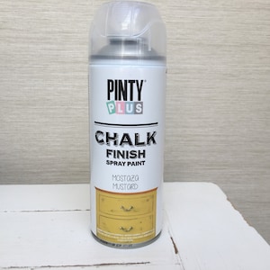 May include: A can of Pinty Plus Chalk Finish spray paint in Mustard. The label displays the brand name, product details, and a graphic of a mustard-coloured dresser. The can has a clear plastic cap.