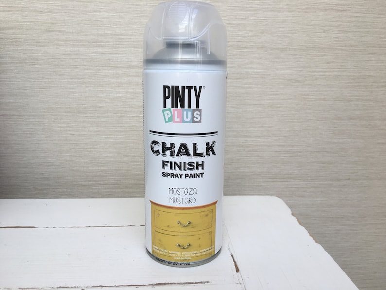May include: A can of Pinty Plus Chalk Finish spray paint in Mustard. The label displays the brand name, product details, and a graphic of a mustard-coloured dresser. The can has a clear plastic cap.