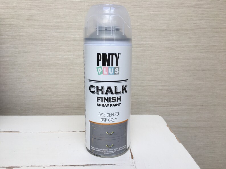 May include: A can of Pinty Plus Chalk Finish spray paint in Ash Grey. The label displays the brand and product information. The can is grey with a clear plastic cap, set against a neutral backdrop.