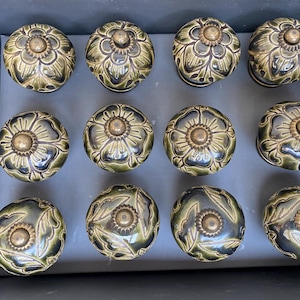 Può includere: Dodici pomelli decorativi per armadi con un design floreale. I pomelli sono in ceramica e hanno una finitura verde scuro e oro.