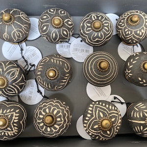 May include: Twelve black and white wooden cabinet knobs with intricate designs. Each knob has a brass centre and a white design on a black background.