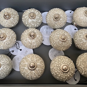 Może przedstawiać: Dwunastu ceramicznych gałek do szuflad z szarą i białą, kropkowaną powierzchnią. Każda gałka ma biały wzór kwiatowy i srebrny metalowy akcent.