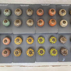 Op de afbeelding: Assortiment van 24 decoratieve kastknoppen met verschillende patronen en kleuren. De knoppen zijn gerangschikt in rijen op een grijze achtergrond. De tekst "Furniture Knobs" is op elke kaart gedrukt.