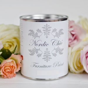 Puede incluir: Una lata blanca de pintura para muebles Nordic Chic con tapa plateada y un dise&ntilde;o floral plateado en la etiqueta.
