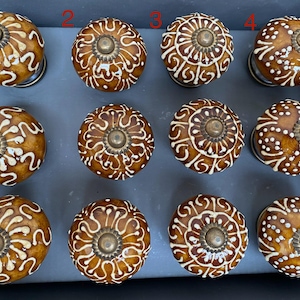 May include: Twelve ceramic cabinet knobs with a brown and white design. The knobs have a raised, circular pattern and a metal accent in the centre.