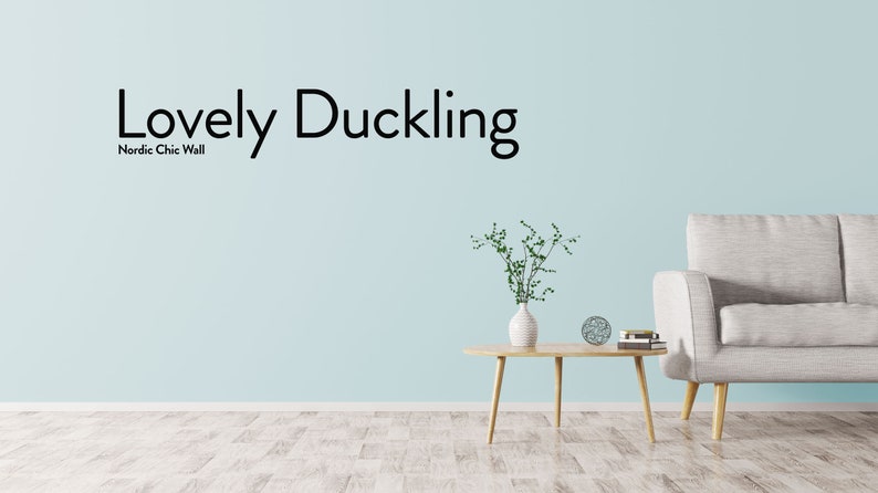 May include: A light blue wall with the text "Lovely Duckling" and "Nordic Chic Wall" in black lettering. A white couch with wooden legs is in the lower right corner of the image. A small wooden table with a vase of green plants and a decorative object is in the center of the image.