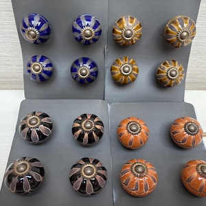 May include: Assortment of ceramic drawer knobs with floral designs. The knobs are in three colors: blue, black, and orange. Each knob has a silver metal center.