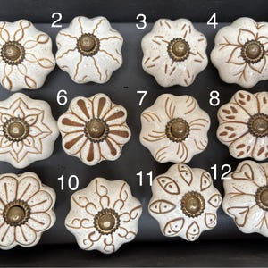 Puede incluir: Doce pomos de armario de cerámica blanca con diferentes diseños marrones. Cada pomo tiene un centro de metal dorado.