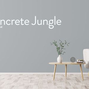 May include: A light gray wall with the text "Concrete Jungle" and the words "Nordic Chic Wall" below it. A white couch with wooden legs sits in front of the wall. A small wooden table with a vase of green plants sits in front of the couch.