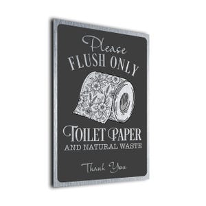 Peut inclure: Panneau rectangulaire en métal avec un fond noir et un bord argenté. Le panneau présente le texte "Please Flush Only" au-dessus d'une illustration d'un rouleau de papier toilette avec des motifs floraux. Le texte "Toilet Paper and Natural Waste. Thank You." est en dessous.