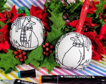 May include: Two white Christmas ornaments with a black and white fox design, accented with a plaid scarf, are displayed among red poinsettias and green holly. The ornaments have decorative lace trim and are suspended by ribbons. Two black markers with the text "SCRIBBLER EXPERIMENT" are also visible.