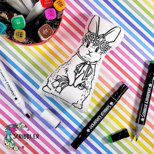 Könnte beinhalten: Ein weißer Plüschhase mit einer Blumenkrone, der einen Blumenstrauß hält. Der Hase ist bereit, mit Markern bemalt zu werden.