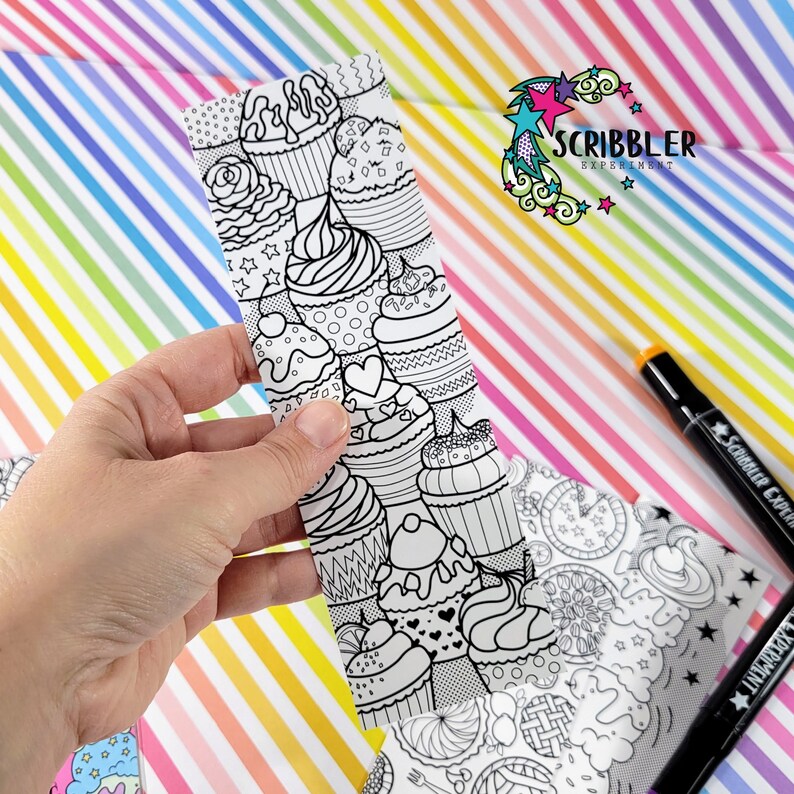 May include: A black and white bookmark with a pattern of cupcakes and hearts. The bookmark is made of paper and is designed to be colored in. The bookmark is part of a set of coloring bookmarks.