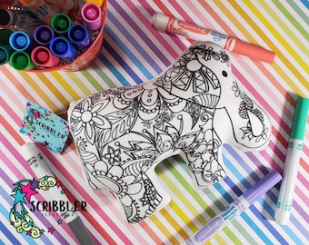 May include: A white plush elephant shaped coloring book with intricate black and white designs. The elephant is lying on a colorful striped background with markers nearby.