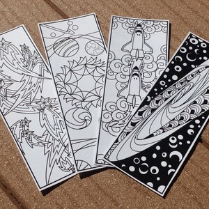 May include: Four black and white bookmark designs featuring space-themed illustrations. The designs include a rocket ship, a galaxy, a planet, and a starburst.