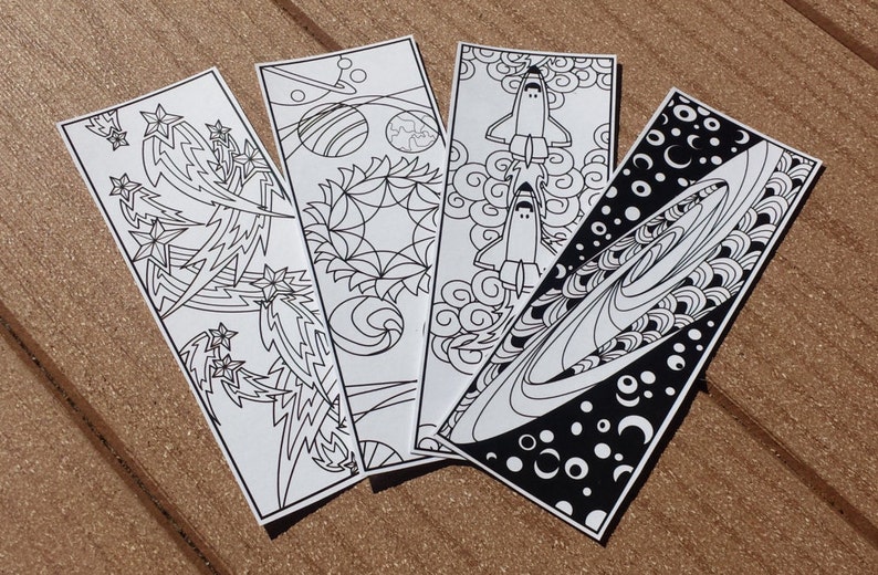 May include: Four black and white bookmark designs featuring space-themed illustrations. The designs include a rocket ship, a galaxy, a planet, and a starburst.