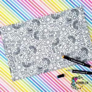 May include: A white fabric placemat with a black and white pattern of menorahs, dreidels, and stars of David. The placemat is on a rainbow striped background. Two black markers with the text "Scribbler Experiment" are on the right side of the image.