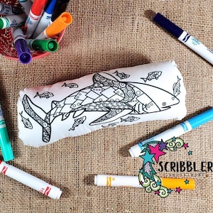 May include: A white pillow with a black and white line drawing of a shark and smaller fish. The pillow is surrounded by colorful markers.