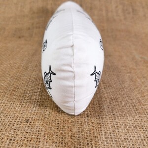 May include: White pillow with a black and white fish pattern. The pillow is shaped like a long oval and is lying on a brown burlap surface.