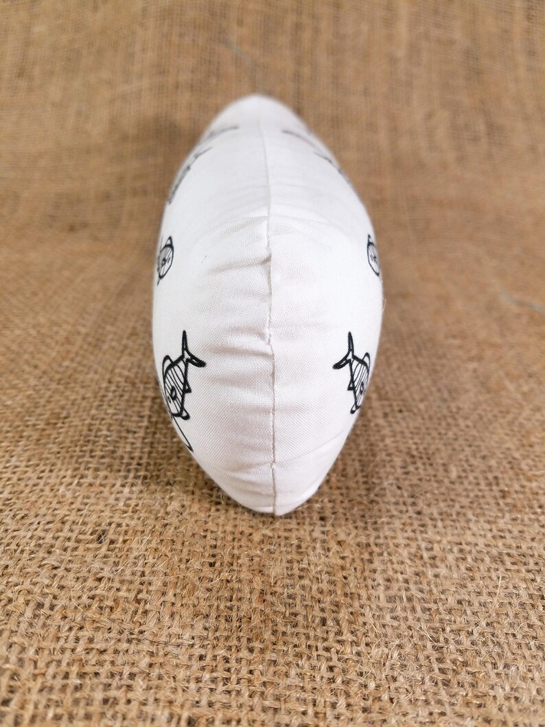 May include: White pillow with a black and white fish pattern. The pillow is shaped like a long oval and is lying on a brown burlap surface.