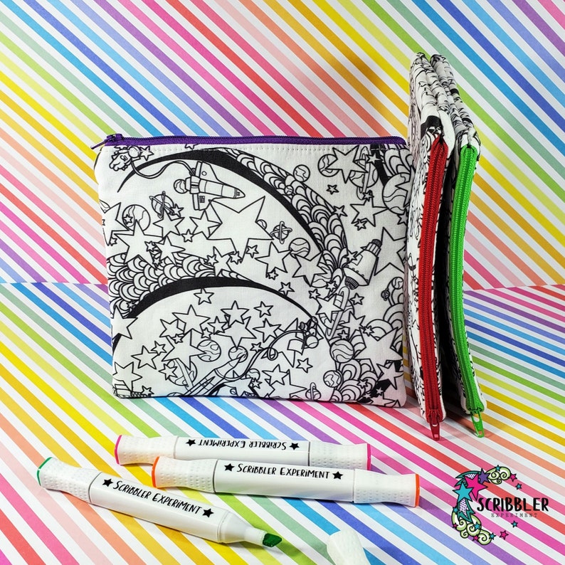 May include: A white zippered pouch with a black and white space-themed design. The pouch is open and three black and white markers are in front of it. The markers have the text "Scribbler Experiment" on them.