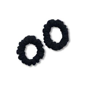 May include: Two black scrunchies made of soft fabric. The scrunchies are in a curled shape and are ideal for holding hair.