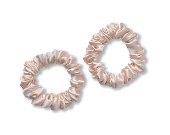 May include: Two light pink satin scrunchies for hair. The scrunchies are made of soft, silky fabric and are designed to be gentle on hair.