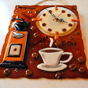 Puede incluir: Un reloj de pared de vidrio marrón con temática de café. La esfera del reloj es blanca con números y manecillas negros. El reloj está rodeado de granos de café, una taza de café, un molinillo de café y las palabras "Espresso Classic", "Chocolate" y "Café".