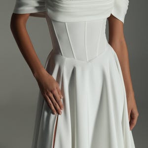 K&ouml;nnte beinhalten: Wei&szlig;es schulterfreies Brautkleid mit eng anliegendem Oberteil und flie&szlig;endem Rock. Das Oberteil hat vertikale N&auml;hte und einen Sweetheart-Ausschnitt. Das Kleid hat einen hohen Schlitz auf der linken Seite. Das Oberteil des Kleides hat eine Perlenverzierung.