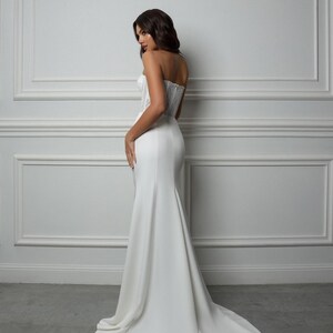 May include: A white strapless wedding dress with a fitted bodice and a flowing skirt. The dress is made of a smooth, satin-like fabric.