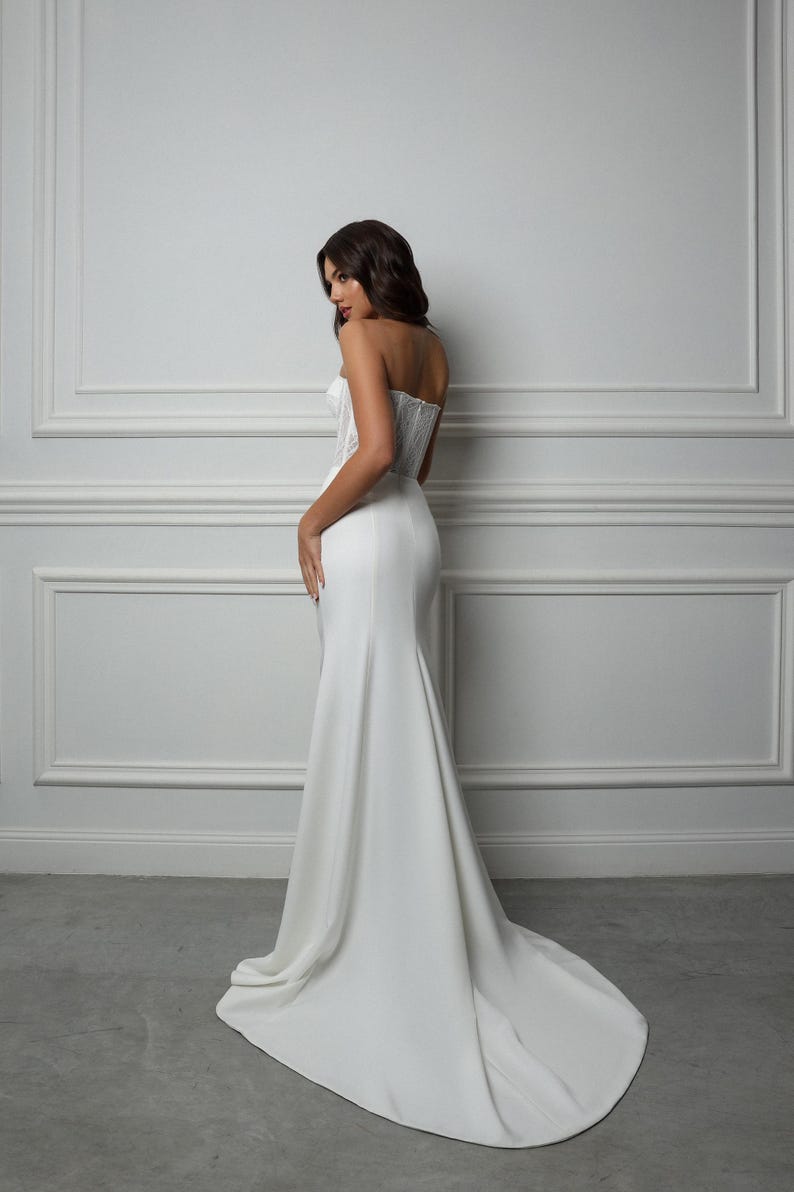 May include: A white strapless wedding dress with a fitted bodice and a flowing skirt. The dress is made of a smooth, satin-like fabric.