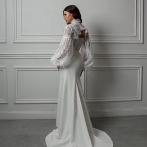 May include: A white wedding dress with a fitted bodice and a flowing skirt. The dress features a lace top with long, puffed sleeves.