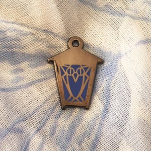 May include: A silver metal lantern charm with a blue owl design. The lantern has a geometric design and the owl has large eyes.