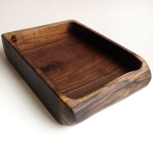 May include: A rectangular wooden tray with a dark brown stain. The tray has a smooth, slightly rounded edge and is made of natural wood.