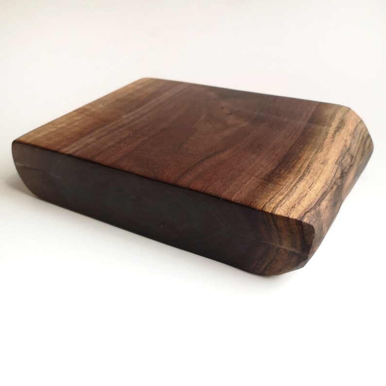 May include: A dark brown wooden chopping board with a live edge. The board is rectangular with rounded corners and a smooth surface.