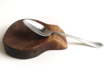 May include: A wooden spoon rest with a natural brown finish. A silver spoon is resting in the spoon rest.