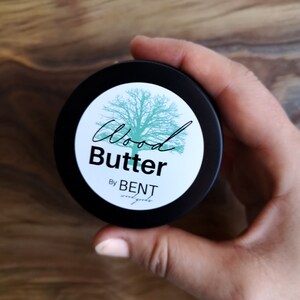 May include: A black jar with a white label that says "Wood Butter" and "By BENT wood goods". The label also features a green tree illustration.