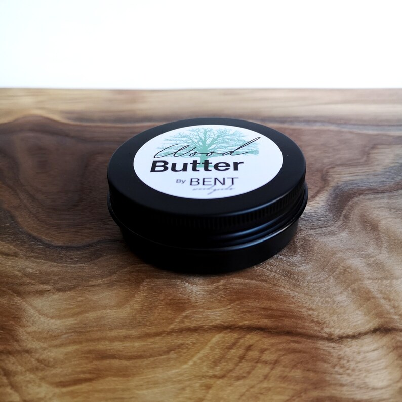 May include: A small black tin container with a white label that reads "Wood Butter by BENT" and a green tree illustration.